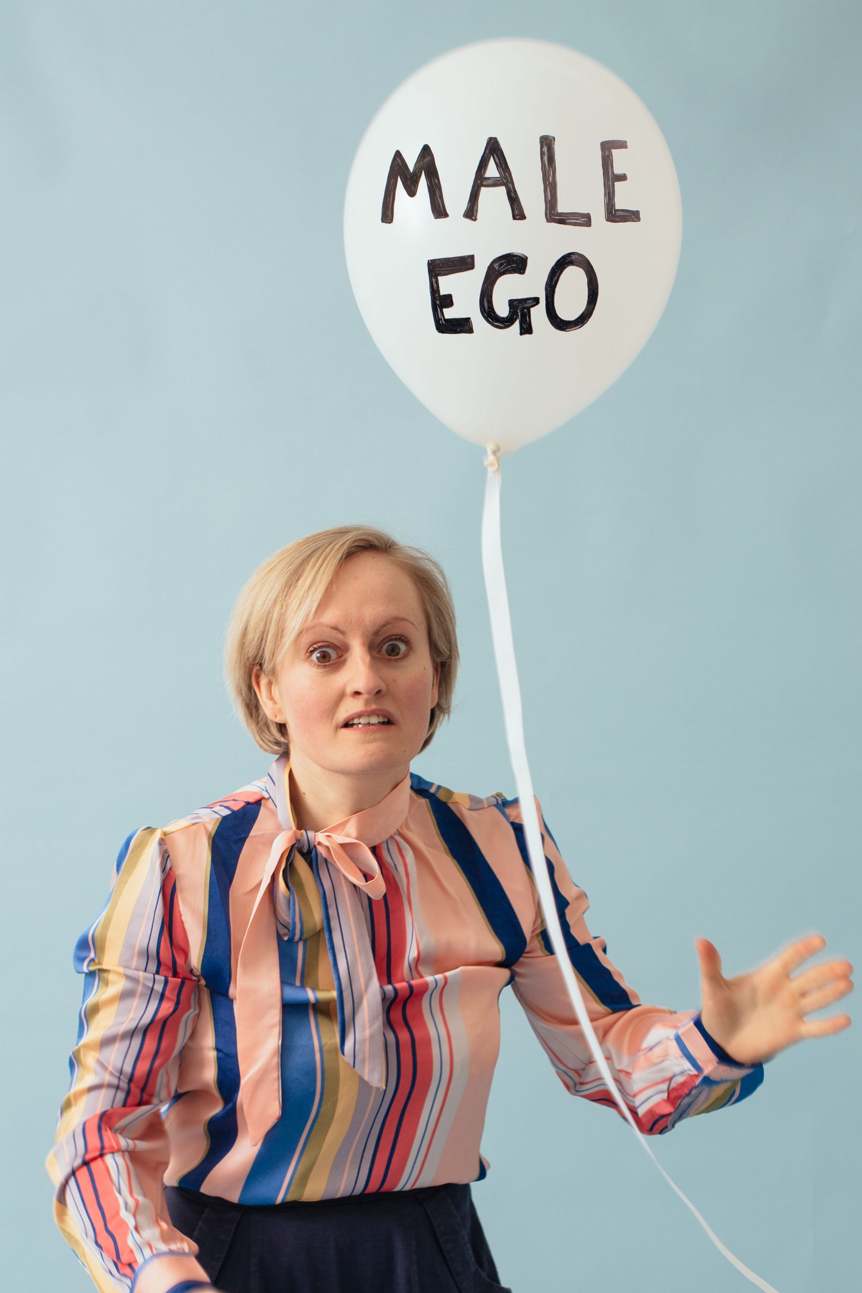 Image of woman holding a balloon with the words Male Ego written on it
