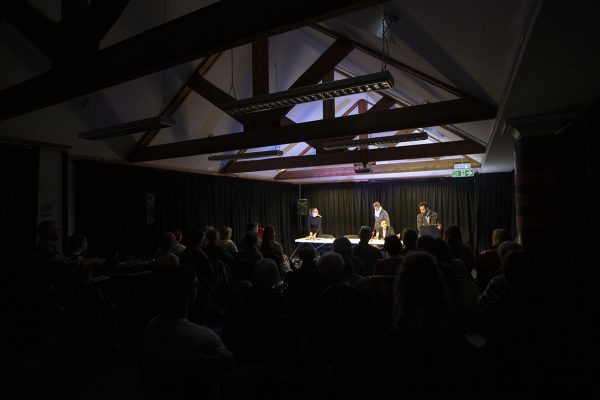 Photo of people seated in a darkened room listening to a talk