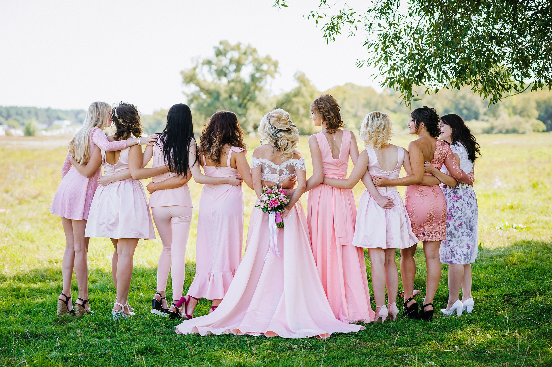 Photo of Bride and bridesmaids, arms interlinked from behind.